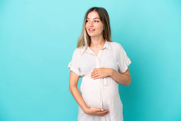 Young Romanian woman isolated on blue background pregnant and happy - Photo, Image
