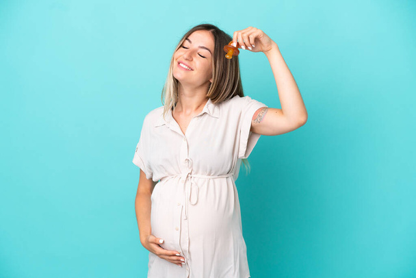 Junge Rumänin isoliert auf blauem Hintergrund schwanger und mit Schnuller - Foto, Bild
