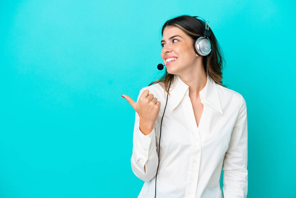 Telemarketer Italian woman working with a headset isolated on blue background pointing to the side to present a product - Foto, Bild
