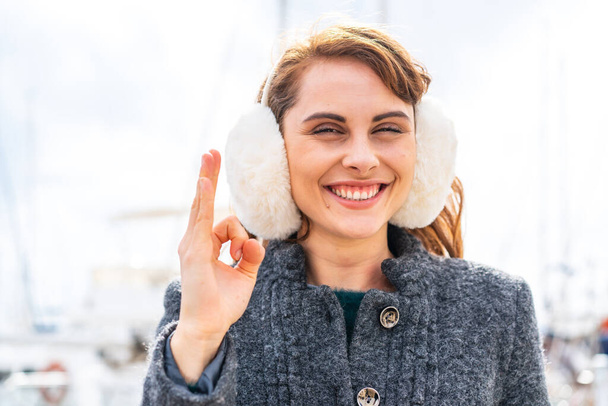 Брюнетка жінка носить зимові муфти на відкритому повітрі, показуючи знак з пальцями - Фото, зображення