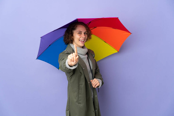Англичанка держит зонтик на фиолетовом фоне, показывая и поднимая палец - Фото, изображение