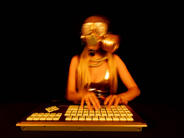 Una mujer con una máscara de gas de oro escribiendo en el ordenador - Foto, imagen
