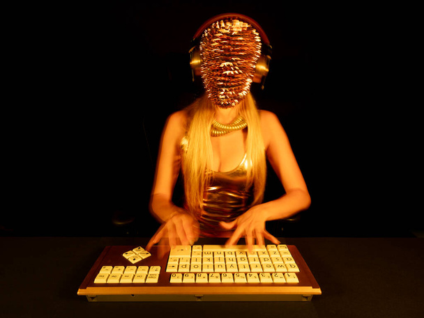 Una mujer con una máscara puntiaguda de oro escribiendo en el ordenador - Foto, imagen