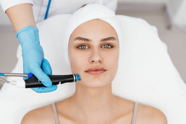 Professional female cosmetologist doing hydra-facial procedure in cosmetology clinic. Doctor using hydra vacuum cleaner. Rejuvenation and cosmetology concept - Photo, Image