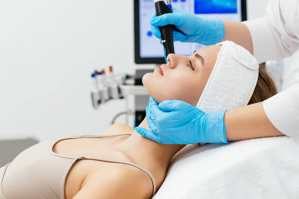 Professional female cosmetologist doing hydra-facial procedure in cosmetology clinic. Doctor using hydra vacuum cleaner. Rejuvenation and cosmetology concept - Photo, Image