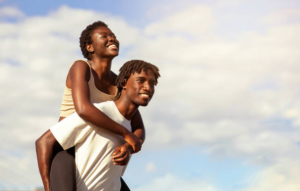 Romantyczna afro-amerykańska para bawiąca się razem podczas treningu sportowego na świeżym powietrzu, młody czarny mężczyzna podpierający swoją szczęśliwą dziewczynę, wesoły mężczyzna i kobieta w odzieży sportowej uśmiechający się i śmiejący - Zdjęcie, obraz
