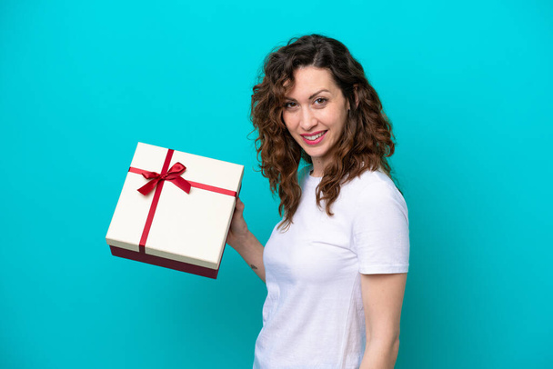 Mladá běloška žena drží dárek izolované na modrém pozadí s úsměvem hodně - Fotografie, Obrázek