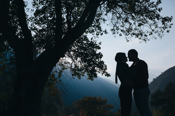 Silueta de una pareja amorosa sobre un fondo de árboles y montañas
 - Foto, Imagen