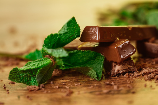 стопка шоколадных кусочков с листком мяты на деревянном фоне
 - Фото, изображение