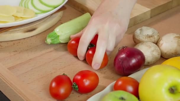 Το χέρι του κοριτσιού παίρνει κόκκινες ντομάτες κοκτέιλ και τις κόβει σε φέτες σε μια ξύλινη σανίδα. Κοντινό πλάνο - Πλάνα, βίντεο