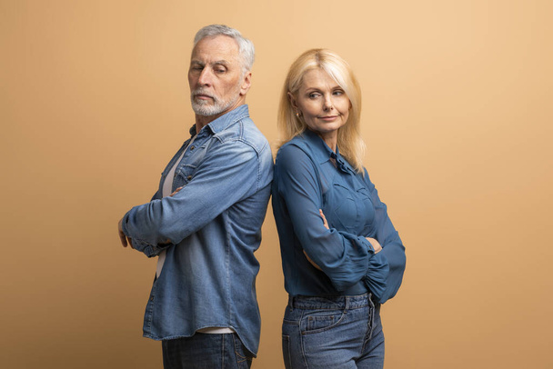 Unhappy marriage, crisis in relationships. Frustrated senior blonde woman wife have quarrel with her furious husband grey-haired man, elderly couple fighting over beige studio background, dont talk - Photo, Image