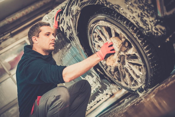 Férfi munkás mosás autó ötvözet kerekek egy autómosó  - Fotó, kép