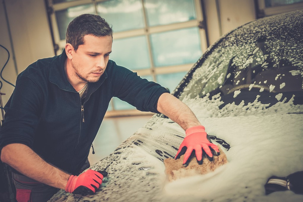 Άνδρας εργαζόμενος πλύσιμο πολυτελές αυτοκίνητο με σφουγγάρι σε ένα πλυντήριο αυτοκινήτων  - Φωτογραφία, εικόνα