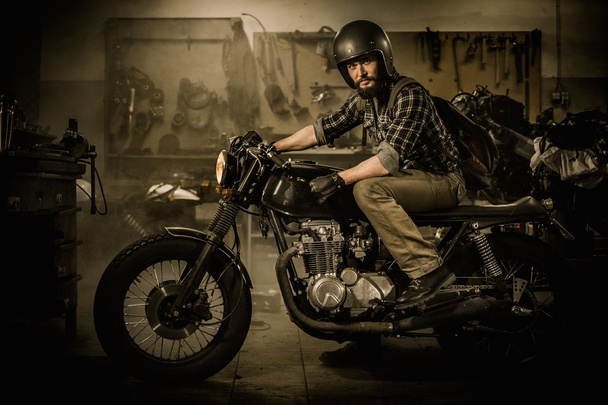 Rider and his vintage style cafe-racer motorcycle in customs garage  - Φωτογραφία, εικόνα