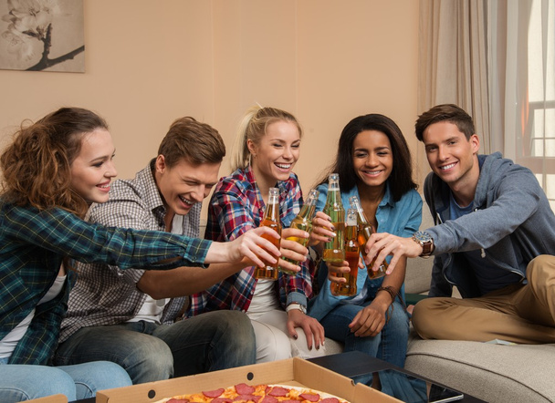 Grupo de jovens amigos multi-étnicos com pizza e garrafas de bebida comemorando em casa interior
 - Foto, Imagem