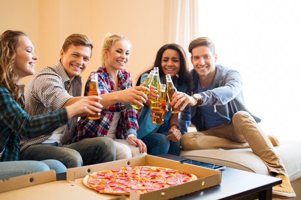 Мультиэтнические друзья с пиццей и бутылками напитков, устраивающие вечеринку
 - Фото, изображение