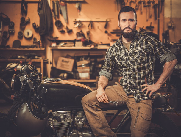 Rider and his vintage style cafe-racer motorcycle in customs garage  - Photo, Image