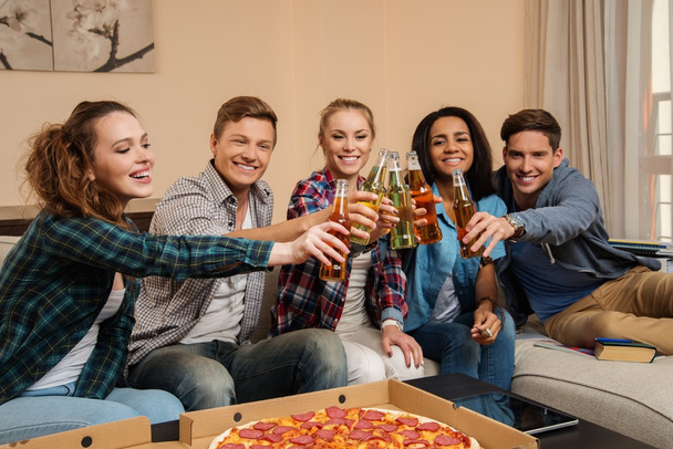 pizza ve şişeler içinde ev iç içmek kutlama ile genç çok etnik gruptan oluşan arkadaş grubu - Fotoğraf, Görsel