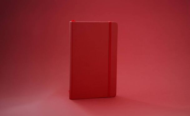 Czerwony skórzany pamiętnik na czerwonym tle. Notatnik z koncepcją elastycznej opaski zakładkowej - Zdjęcie, obraz