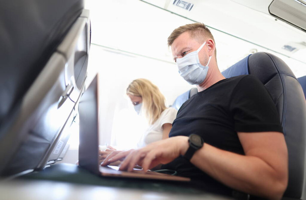 Des hommes et des femmes portant des masques de protection travaillant sur des ordinateurs portables dans la cabine d'un avion. Télétravail pendant la covid19 concept de pandémie - Photo, image