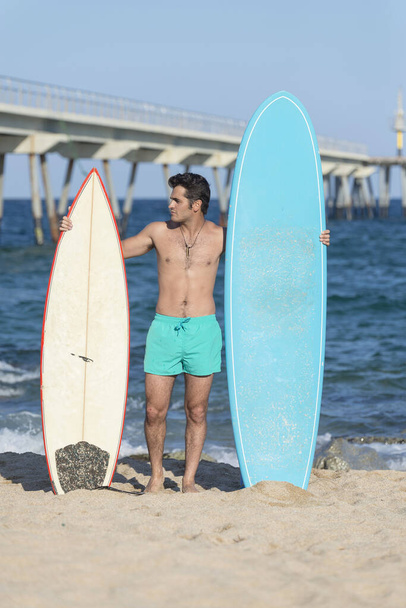 Un surfista senza maglietta in piedi sulla spiaggia con una tavola da surf - guardando in basso - Foto, immagini