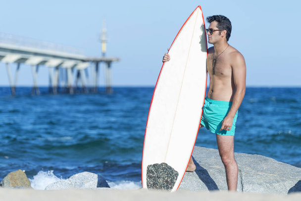 Plajda elinde sörf tahtası olan çıplak bir sörfçü. - Fotoğraf, Görsel