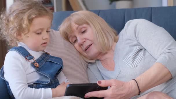Una abuela feliz visita a su nieta, juegan juntos y usan un teléfono inteligente. Amor de diferentes generaciones en la familia. - Metraje, vídeo