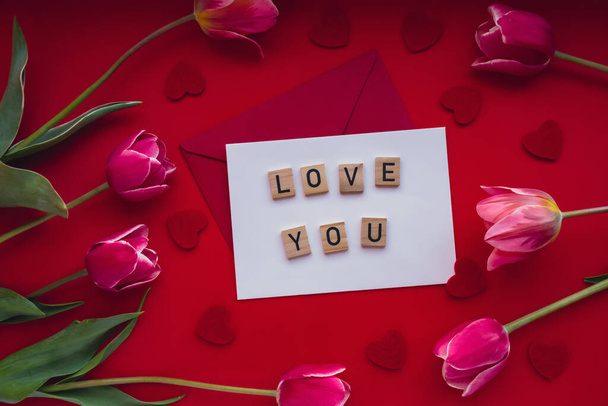 LOVE YOU γραπτό μήνυμα σε φάκελο με όμορφο ροζ τουλίπα μπουκέτο σε κόκκινο φόντο. Πρότυπο mock up για τις διακοπές ευχετήρια κάρτα. Ερωτικό ειδύλλιο Ημέρα του Αγίου Βαλεντίνου - Φωτογραφία, εικόνα