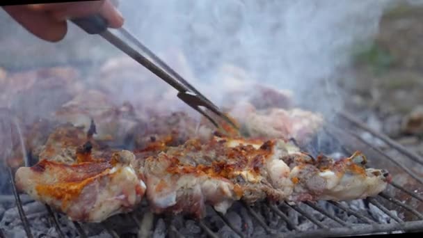 Közelkép az emberi kéz főzés grill fém rács szabadban, vidéken. Grill friss marhahús szeletek. Hagyományos keleti étel, sashlik. Grill faszénen és lángon, piknik, utcai kaja - Felvétel, videó