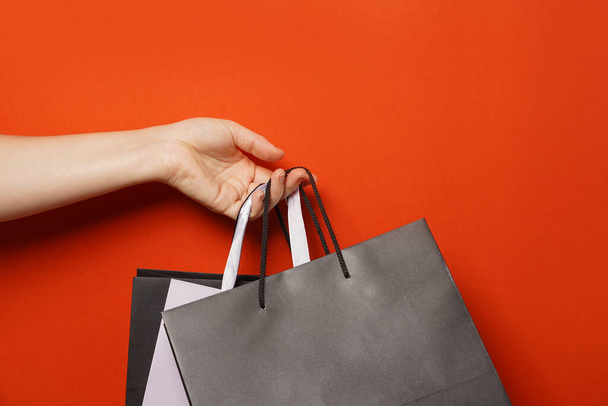 ビッグセール,低価格。 女性の手は赤い背景,コピースペースに黒い紙のショッピングバッグを保持しています. ブラックフライデーのコンセプト - 写真・画像