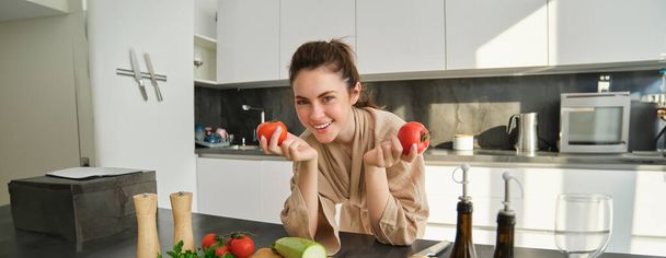 Muotokuva naisen ruoanlaitto kotona keittiössä, tilalla tomaatit, valmistella herkullinen tuore ateria vihanneksia, seisoo lähellä leikkuulauta. - Valokuva, kuva