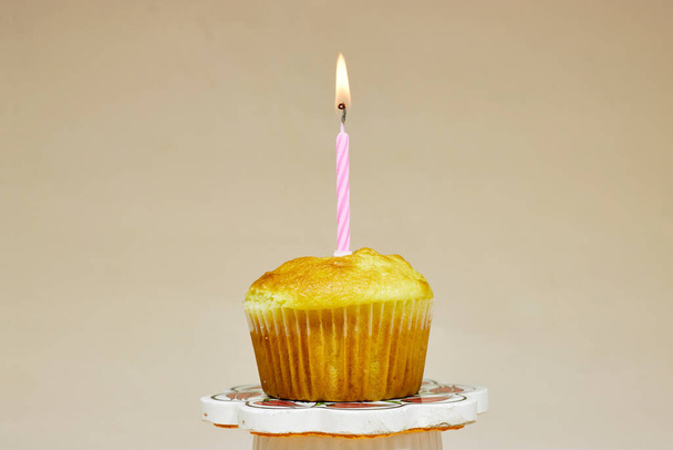 Verjaardag cupcake op het podium staan met een verjaardagstaart kaars op een beige achtergrond - Foto, afbeelding