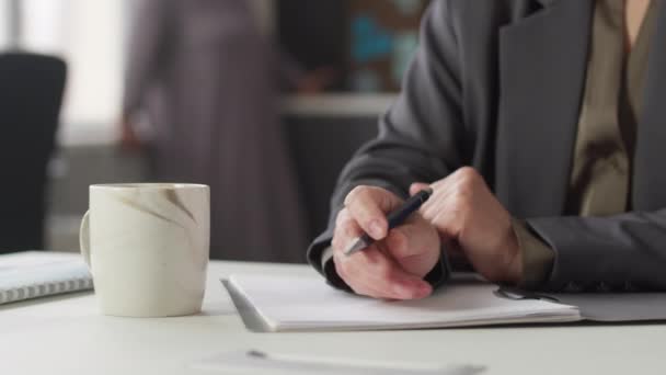 Cropped shot of unrecognizable businesswoman signing documents and drinking hot tea or coffee from mug sitting at work desk in office - Footage, Video