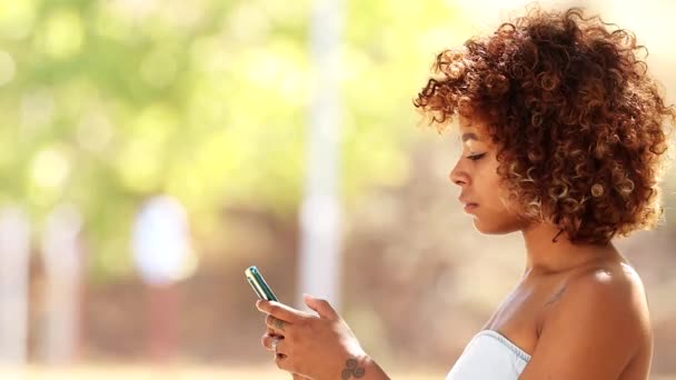 latin afro american young woman smiling looking at camera with mobile phone outdoors - Footage, Video
