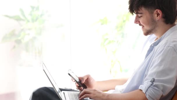 Nuori mies kannettavan tietokoneen ja matkapuhelimen profiilin kopio-tilaa - Materiaali, video