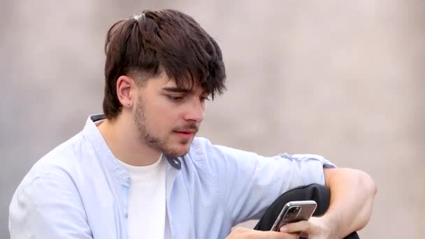 jeune homme dans la rue avec téléphone portable regardant et souriant à la caméra - Séquence, vidéo
