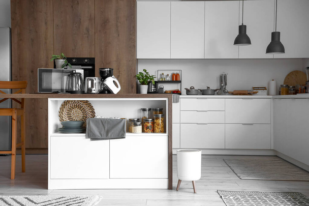 Интерьер светлой кухни с современной техникой на деревянном столе - Фото, изображение