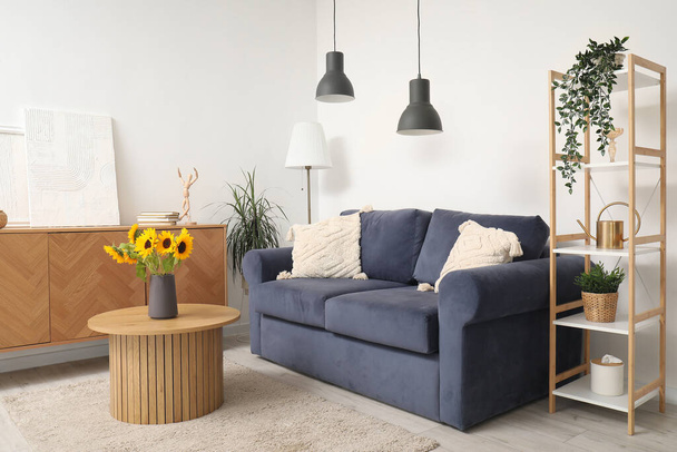 Blaues Sofa und Vase mit schönen Sonnenblumen auf Holztisch im Wohnzimmer - Foto, Bild