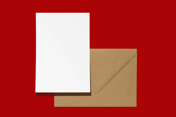 Joulukirjeen mallinnus. Tyhjä valkoinen tyhjä sivu ja ruskea paperi kirjekuori punaisella taustalla. Postikortti, terveisiä ja kiitos kortti malli. - Valokuva, kuva