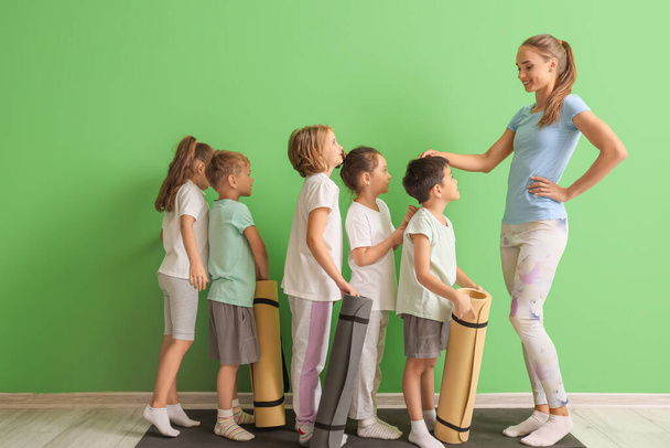 Instructora de yoga femenina y grupo de niños pequeños cerca de la pared verde - Foto, imagen