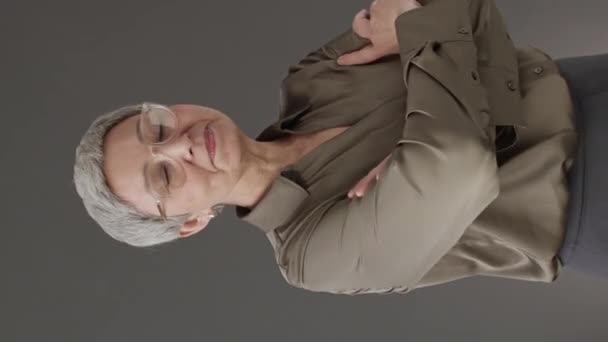 Retrato vertical mediano de una exitosa mujer de negocios caucásica de mediana edad posando con las manos dobladas sobre un fondo gris oscuro - Metraje, vídeo