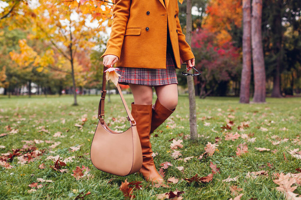 Orange knee high boots. Fashionable woman wearing stylish blazer plaid mini skirt walking in fall park with beige handbag among leaves. Copy space - Photo, Image