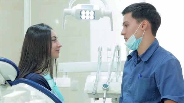 Πορτρέτα από τον οδοντίατρο και τον ασθενή. Ο οδοντίατρος λέει στον ασθενή μια νεαρή γυναίκα, στη συνέχεια, γυρίζουν και τα δόντια χαμόγελο απευθείας στην κάμερα - Πλάνα, βίντεο