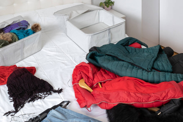 Foto horizontal, de una habitación con ropa de invierno acostada sobre la cama, para ser recogida dentro de las cajas de tela. Haciendo cambio de armario. - Foto, Imagen
