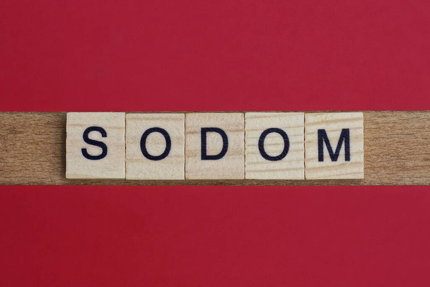 text slovo sodoma z šedých dřevěných písmen s černým písmem na červeném stole - Fotografie, Obrázek