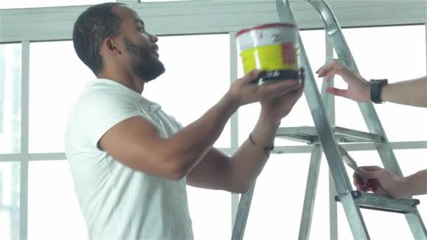 Ζωγραφική, μετεγκατάσταση και επισκευές στο διαμέρισμα. Δύο εργαζόμενοι κάνει επισκευές σε ένα νέο διαμέρισμα. Ένας άντρας παίρνει το χρώμα σε ένα άλλο άτομο στη Σκάλα - Πλάνα, βίντεο