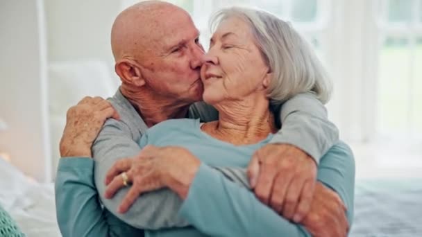 Seniorenpaar, knuffel en kus in de slaapkamer, zorg en gesprek samen thuis. Liefde, oudere man en gelukkige vrouw in bed, omhelzing en verbondenheid voor steun, relatie en verbintenis aan het huwelijk. - Video