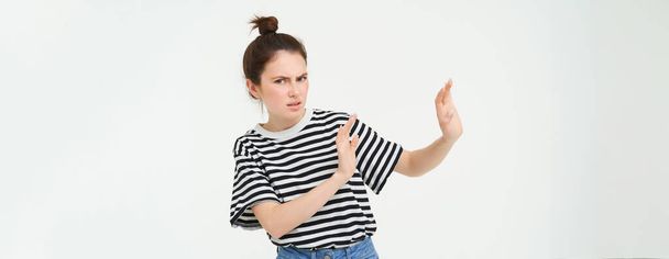 Image of woman expressing aversion, dislike something, looks apalled, extends hands forward in defensive gesture, rejecting, refusing, standing over white background. - Photo, Image