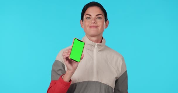 Nő, telefon és mosoly zöld képernyőn stúdió arc, mockup vagy izgatott promo a kék háttér. Lady, modell és show okostelefon tréningruha sport app, logó és márka portré. - Felvétel, videó