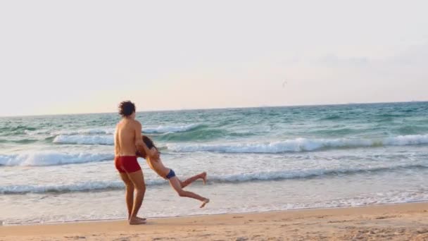 幸せな父親と息子がビーチで一緒に遊んでいました. 父親は息子を回して 手を握った。 フリーで幸せな陽気なライフスタイル - 映像、動画